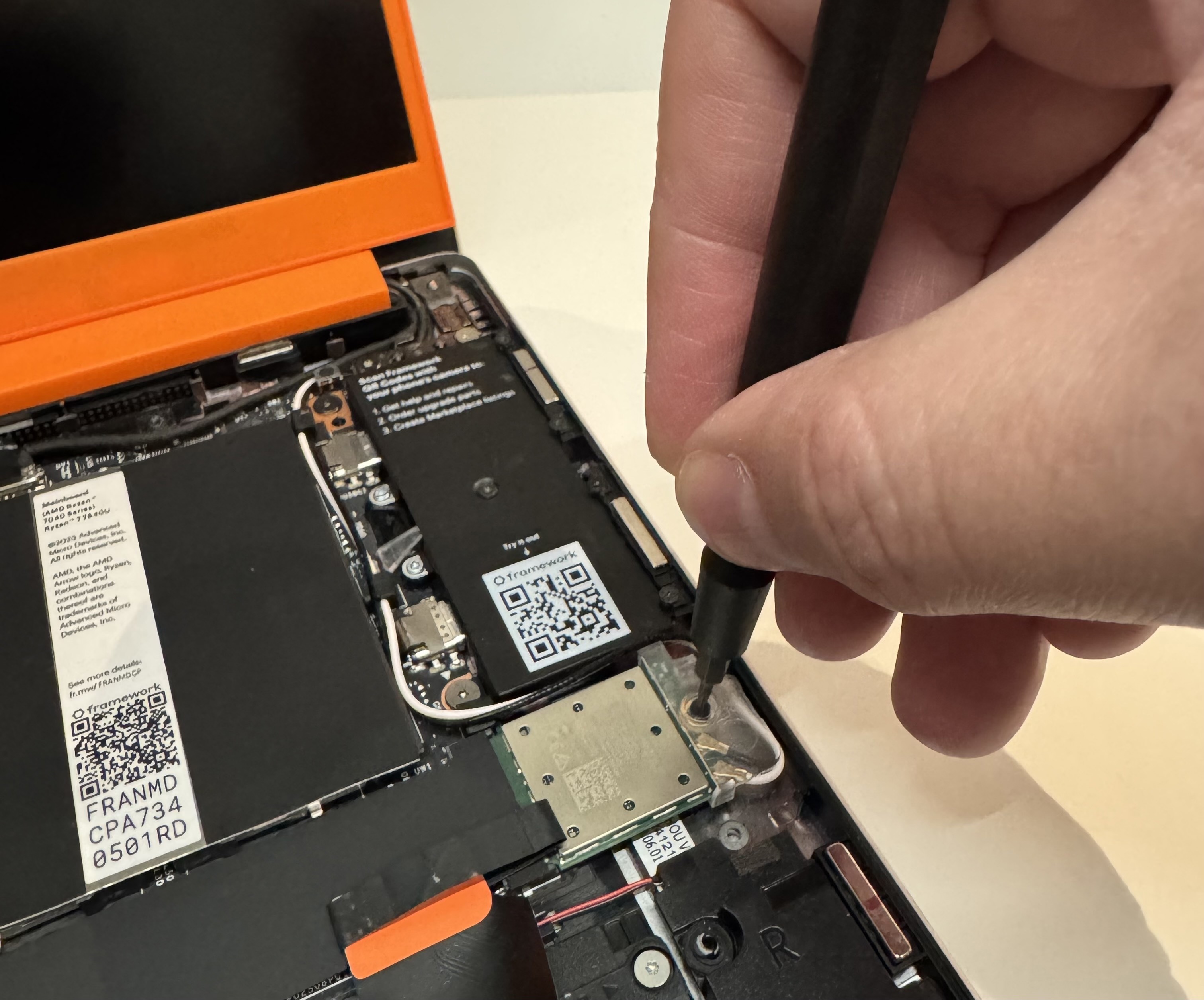 A hand holding a screwdriver, securing a WiFi card into a Framework laptop