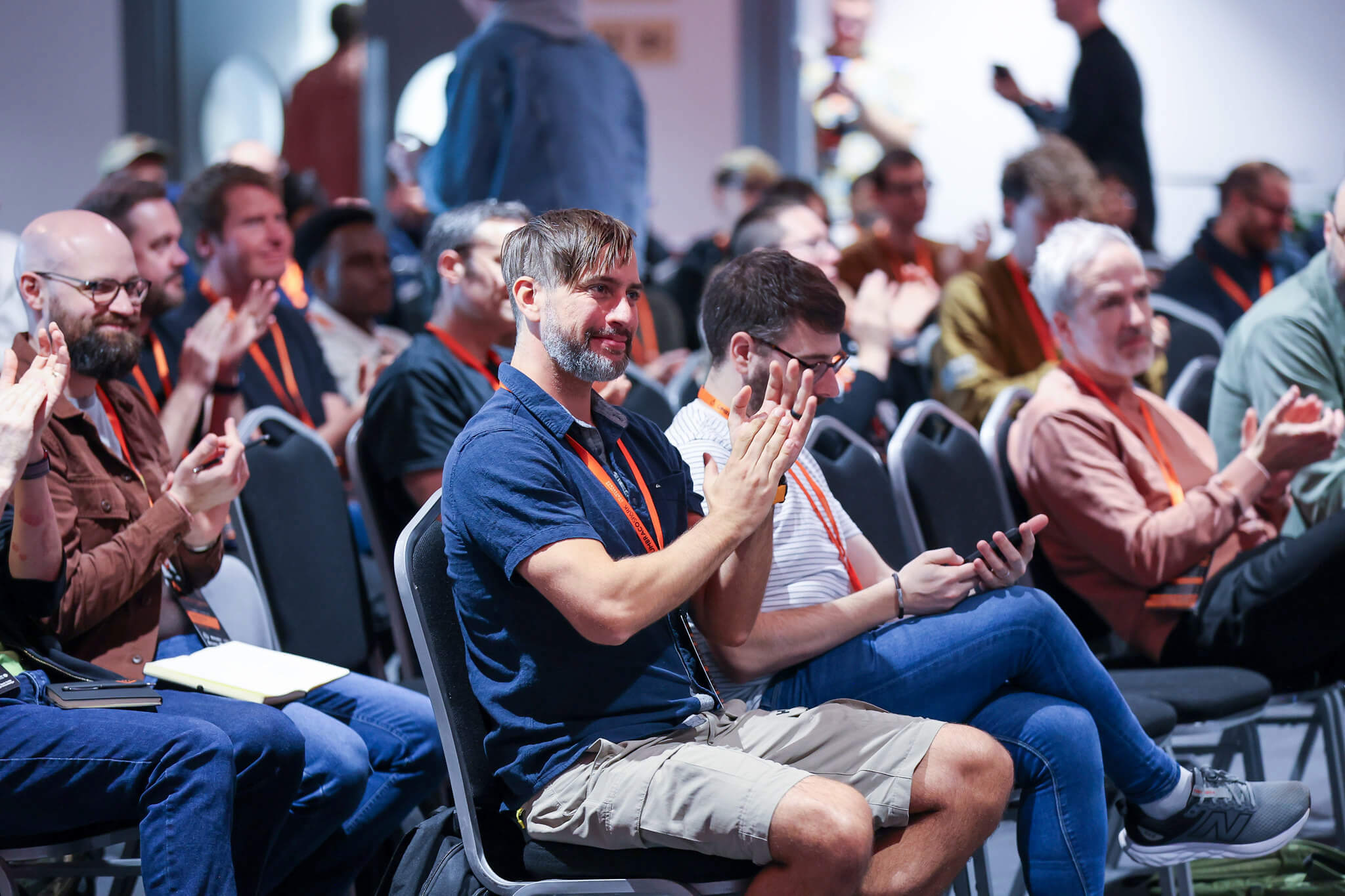 Attendees with orange lanyards sit in rows at Umbraco Spark 2026, smiling and applauding during a talk.